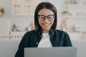 Smiling woman wearing glasses working or learning online at laptop at home. Remote job, elearning