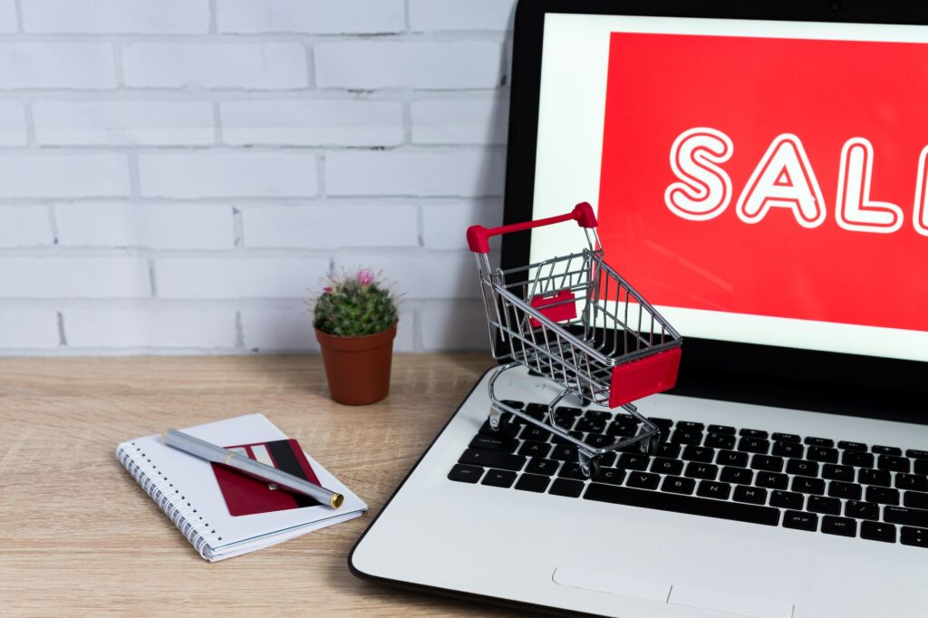 E-commerce concept. Laptop with red inscription ant toy trolley on wooden table